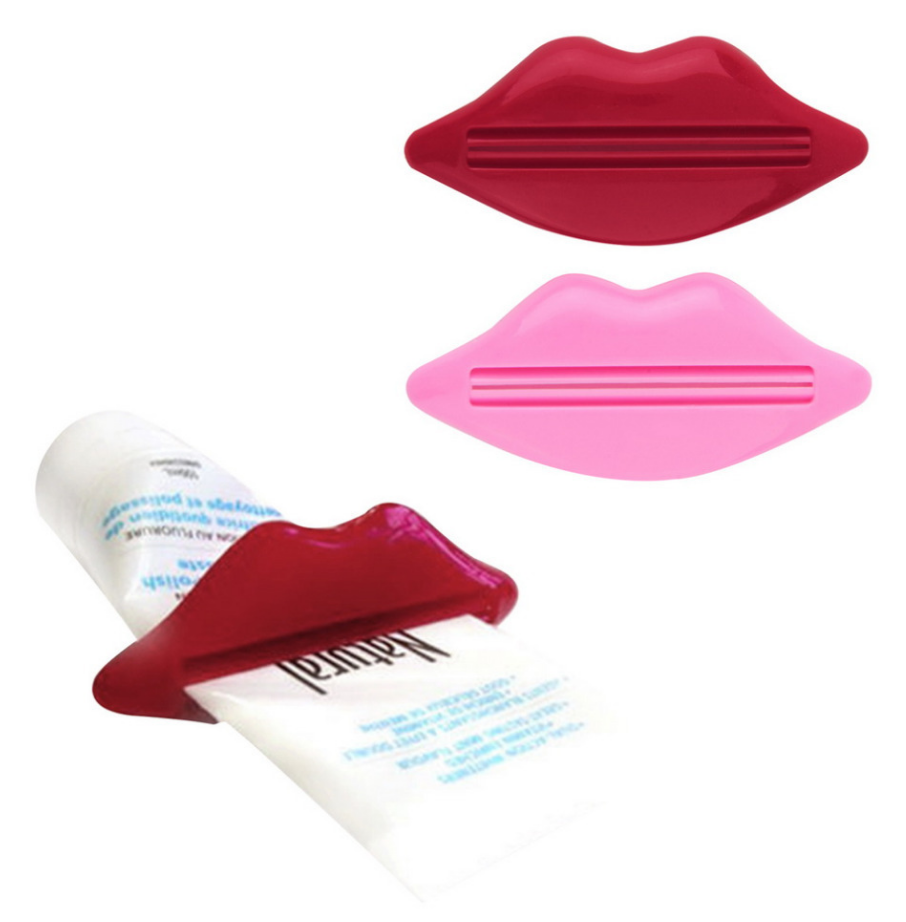 Two plastic toothpaste squeezers shaped like a pair of lips, one dark red and one pink, with the red one clamped onto a tube of toothpaste.