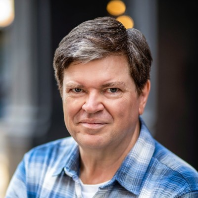 Yann LeCun, a man with short brown hair wearing a blue plaid shirt, smiles at the camera.